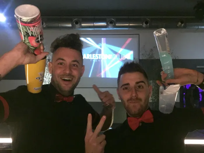 Due barman con papillon rosso alzano le bottiglie al Charleston Club