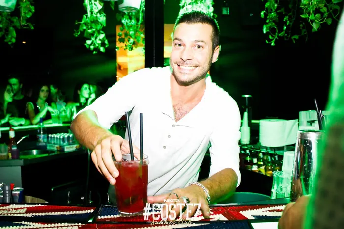 Un barman sorridente serve un cocktail rosso al bancone di una discoteca