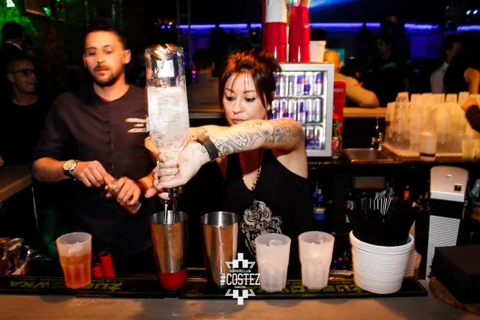 Una bartender versa da una bottiglia capovolta nel tin durante una serata