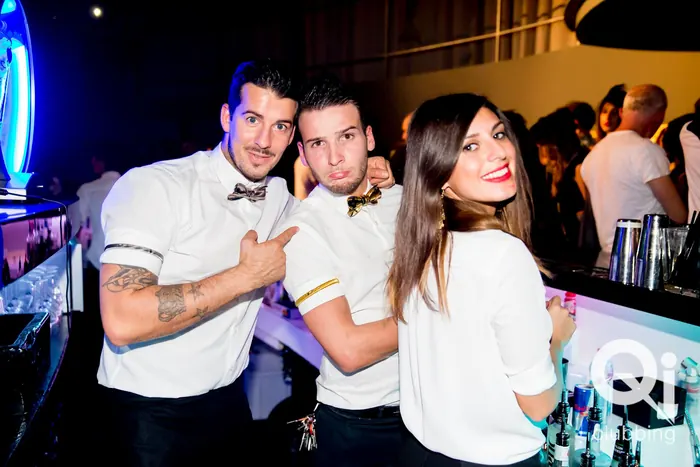 Tre barman in camicia bianca e papillon in posa al bancone del Qi Clubbing