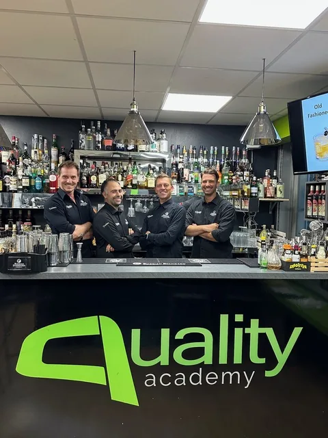 Quattro trainer di Quality Academy in divisa nera dietro al bancone con il logo verde della scuola